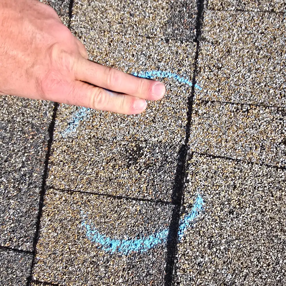 Hail impacts on asphalt shingles circled in blue chalk during a JBS Roofers inspection